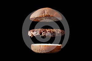 Flying burger with bun and patty isolated on black background