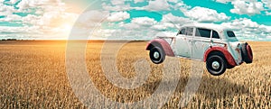 Flying car soars into the sky. Retro automobile hovers in the air above a golden wheat field on the background of blue sky.