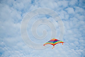 Flying colorful kite on cloudy blue sky background