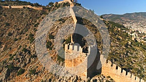 Flying copter over historic Alanya fortress walls on rocky hills at the background of town panorama. Antalya Province