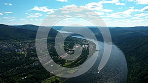 Flying drone along wide river and mountains, hydroelectric power plant in background. Height of bird's flight