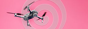 Flying drone with camera on pink background with copy space. Airborne quadcopter. Also known as a drone or UAV.