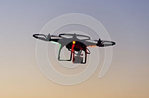 Flying drone with camera on the sky at sunset