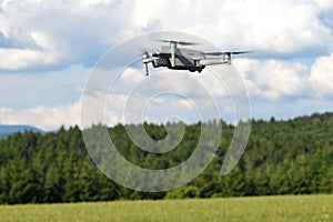 Flying drone quadcopter closeup side view with forest and field
