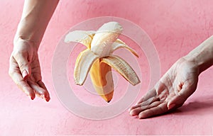 flying or falling fruit - Open floating banana on pink background with womans hands. Tricking or charity or donation concept
