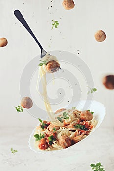 Flying food. Levitation of pasta fettuccine with meatballs, tomato sauce, basil on white background