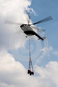 Flying helicopter carrying small vehicle with cloudy blue sky as background