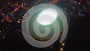 Flying high above the illuminated stadium, night city lights