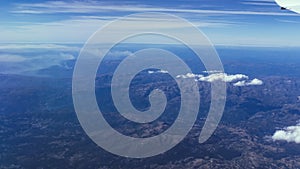Flying high view from brown mountains through the plain Spain with some clouds view from an airplane window