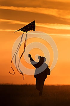 Flying a kite. The boy runs across the field with a kite. Bright sunset