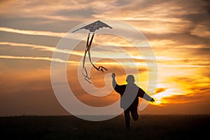 Flying a kite. The boy runs across the field with a kite. Silhouette of a child against the sky. Bright sunset