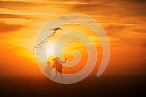 Flying a kite. Girl and boy fly a kite in the endless field. Bright sunset. Silhouettes of people against the sky