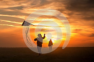 Flying a kite. Girl and boy fly a kite in the endless field. Bright sunset. Silhouettes of people against the sky