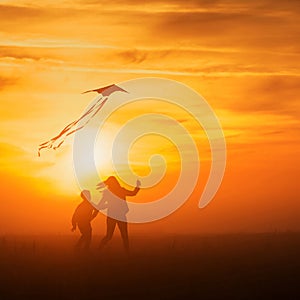 Flying a kite. Girl and boy fly a kite in the endless field. Bright sunset. Silhouettes of people against the sky