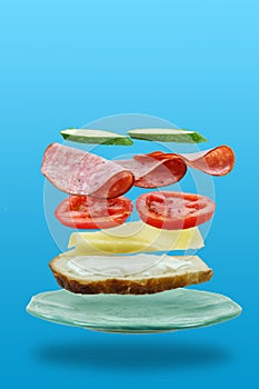 Flying layers of sandwich with ham, cheese, and vegetables on the blue background