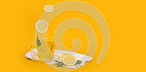 Flying lemon slices fall into a glass with a drink. Mug with tea on a white towel with lemon, mint leaves and currants on a yellow