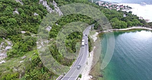 Flying over an asphalt road running along the sea coast. Vehicles are driving along the road