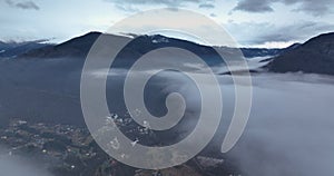 Flying over the clouds on top of a small village with a mountain backdrop.