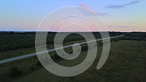 Flying over a countryside road and green fields, aerial view. Clip. Endless flat terrain covered by summer bushes and