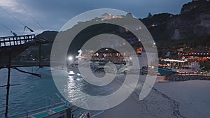 flying over evening coast of the tourist beach of Melasti on island of Bali. Beach restaurants with neon lights swimming