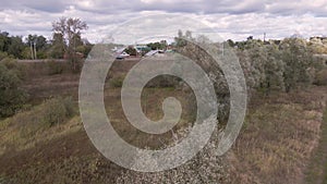 Flying over a field with green trees and moving cars in the background.