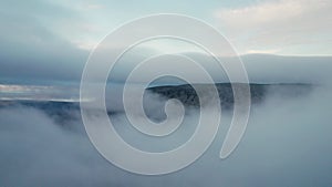 Flying over low hanging clouds with side view of steep rocky mountain cliff in the Scandinavian landscape