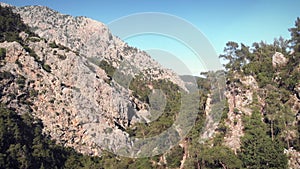 Flying over rocky mountain range ridge. Huge rocky mountains and green woodland from bird`s eye view.  Adventure road trip in summ