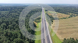 flying over a two-way road between forests and fields along which many cars travel