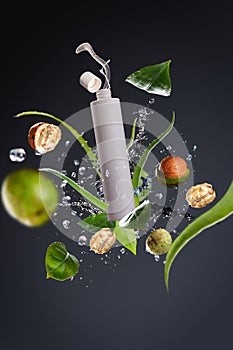 Flying packaging Cosmetic product with splashes and ingredients elements of nuts, aloe and greenery leaves on a gray background. P