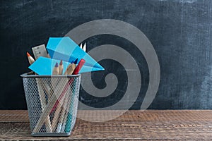 Flying paper plane stucked in a bucket with coloured pencils on wooden table with school supplies. Back to school and education co