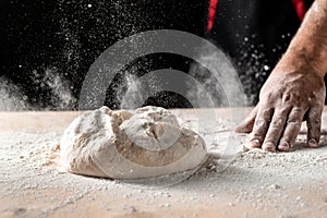 Flying pizza dough with flour scattering in a freeze motion of a cloud of flour midair on black. Cook hands kneading dough. copy