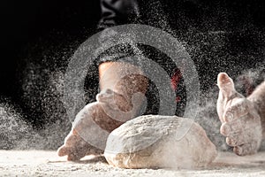 Flying pizza dough with flour scattering in a freeze motion of a cloud of flour midair on black. Cook hands kneading dough. copy