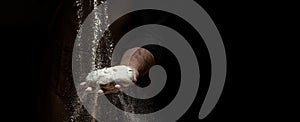 Flying pizza dough with flour scattering in a freeze motion of a cloud of flour midair on black. Cook hands kneading dough. copy