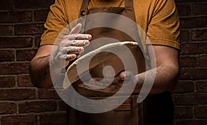 Flying pizza dough with flour scattering in a freeze motion of a cloud of flour midair on black. Cook hands kneading dough. copy