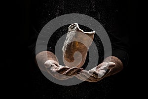 Flying pizza dough with flour scattering in a freeze motion of a cloud of flour midair on black. Cook hands kneading dough. copy