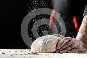 Flying pizza dough with flour scattering in a freeze motion of a cloud of flour midair on black. Cook hands kneading dough. copy