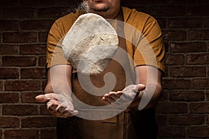 Flying pizza dough with flour scattering in a freeze motion of a cloud of flour midair on black. Cook hands kneading dough. copy