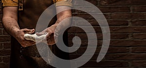 Flying pizza dough with flour scattering in a freeze motion of a cloud of flour midair on black. Cook hands kneading dough. Long