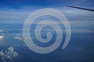 Flying on the plane seeing shades of tinted blue sky horizon background and sunrise light on white cloud with airplane wing