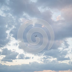 Flying plane in the sky with clouds at sunset as a background