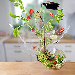 Flying salad, lettuce, tomatoes, cucumbers and radishes are falling with oil and vinegar splashes into a bowl in the kitchen,