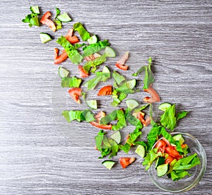 Flying salad on wood to bowl, sliced cucumber tomato salad leaves, green onion, flax seeds