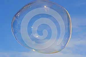 Flying soap bubble with reflection of the blue sky
