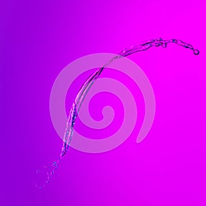 Flying splash transparent liquid or water on lilac color background in neon light. Minimalism, art, fashion