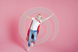 Flying superhero. Funny young woman in the image of a superhero to the rescue. Pink background