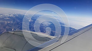 Flying and traveling abroad, bird eye view from airplane window on the jet wing on cloudy blue sky iceberg mountain aboard morning