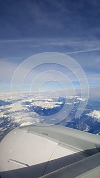 Flying and traveling abroad, bird eye view from airplane window on the jet wing on cloudy blue sky iceberg mountain aboard morning