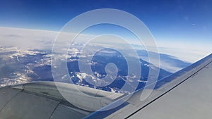 Flying and traveling abroad, bird eye view from airplane window on the jet wing on cloudy blue sky iceberg mountain aboard morning