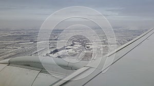 Flying and traveling abroad, bird eye view from airplane window on the jet wing on cloudy blue sky iceberg mountain snow field