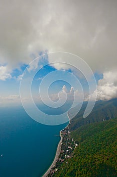 Flying under the clouds along the turquoise sea and the green coast with many hotels. aerial photo from a paraglider, summer